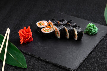 sushi rolls laid out on a dark background decorated with bamboo leaves and chopsticks