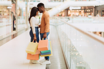 Cheerful young black couple hugging and holding shopping bags