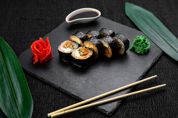 sushi rolls laid out on a dark background decorated with bamboo leaves and chopsticks