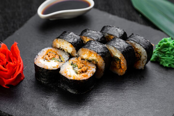 sushi rolls laid out on a dark background decorated with bamboo leaves and chopsticks