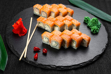 sushi rolls laid out on a dark background decorated with bamboo leaves and chopsticks