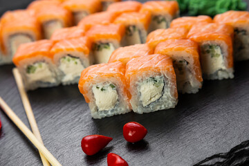 sushi rolls laid out on a dark background decorated with bamboo leaves and chopsticks