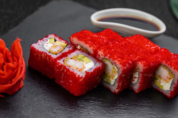 sushi rolls laid out on a dark background decorated with bamboo leaves and chopsticks