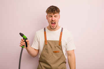 young cool man shouting aggressively, looking very angry. gardener and hose concept