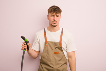young cool man feeling sad and whiney with an unhappy look and crying. gardener and hose concept