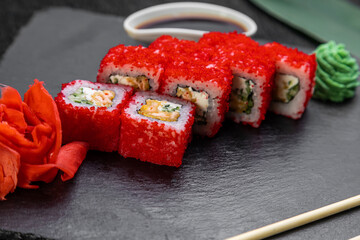 sushi rolls laid out on a dark background decorated with bamboo leaves and chopsticks