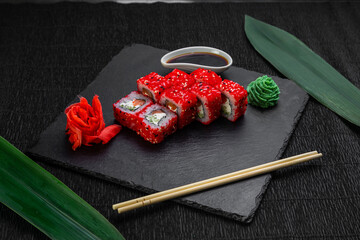 sushi rolls laid out on a dark background decorated with bamboo leaves and chopsticks