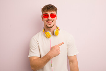 young cool man looking excited and surprised pointing to the side. sunglasses and headphones