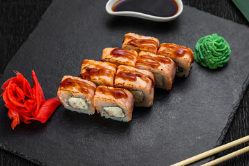 sushi rolls laid out on a dark background decorated with bamboo leaves and chopsticks
