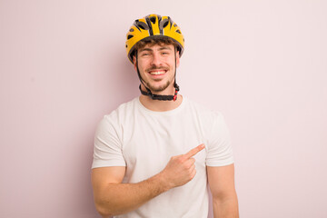 young cool man smiling cheerfully, feeling happy and pointing to the side. bike concept