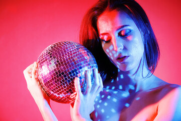 Gorgeous woman posing with disco ball and effect lighting in front of pink background in studio