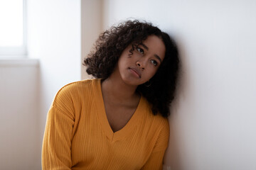 Depressed young black woman sitting near wall alone, having mental or psychological problem at home