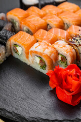 sushi rolls laid out on a dark background decorated with bamboo leaves and chopsticks