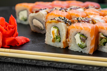 sushi rolls laid out on a dark background decorated with bamboo leaves and chopsticks