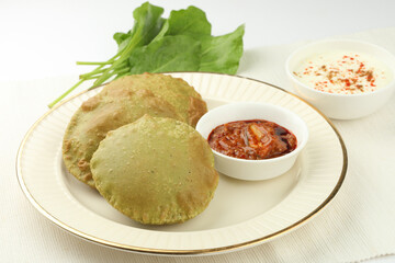 Palak poori served with yogurt made from spinach puree and wheat flour ,popular Indian vegetarian breakfast, with fresh spinach leaves.