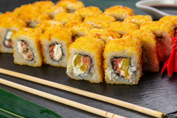 sushi rolls laid out on a dark background decorated with bamboo leaves and chopsticks