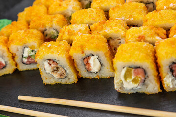 sushi rolls laid out on a dark background decorated with bamboo leaves and chopsticks