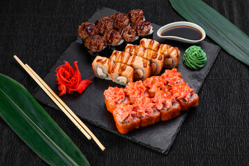 sushi rolls laid out on a dark background decorated with bamboo leaves and chopsticks