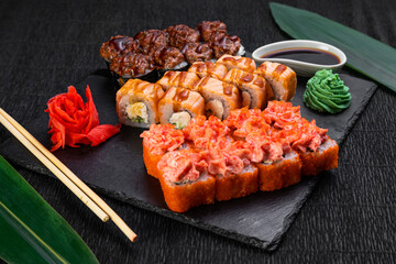 sushi rolls laid out on a dark background decorated with bamboo leaves and chopsticks
