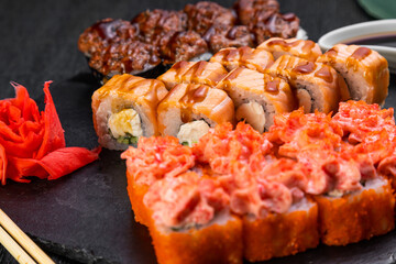 sushi rolls laid out on a dark background decorated with bamboo leaves and chopsticks