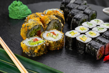 sushi rolls laid out on a dark background decorated with bamboo leaves and chopsticks