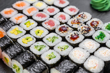 sushi rolls laid out on a dark background decorated with bamboo leaves and chopsticks