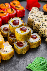 sushi rolls laid out on a dark background decorated with bamboo leaves and chopsticks
