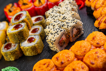sushi rolls laid out on a dark background decorated with bamboo leaves and chopsticks