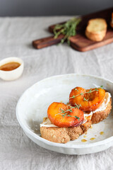Summer Breakfast - toast (sandwich, bruschetta) with grilled peaches, cream cheese (ricotta, mascarpone), thyme and honey on beige linen tablecloth. Selective focus
