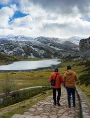 Fototapeta na wymiar Two men walking towards a lake with snow-capped mountains in the background.