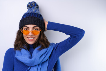 Young woman in a blue golf turtleneck, hat and scarf, sunglasses, on a white background, cheerful in a good mood