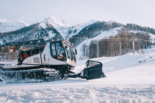 Sochi, Estosadok, Russia, 31 March 2021: Snowcat 'Prinoth' a tracked large heavy machine at work preparing ski slopes with snowy mountains in the background.
