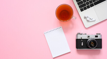 Notepad, cup of tea, laptop and vintage camera on a pink background. Workplace of a creative person. Flat lay, copy space.