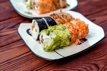 Several sushi on a white plate standing on a brown wooden background
