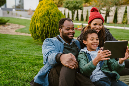 Black Family Using Tablet Computer While Resting Together On Backyard