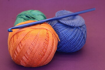 three balls of knitting threads for hobbies and creativity and needlework with a hook on a purple background