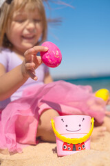 Happy kid on Easter egg hunt on the sandy beach. Happy Easter holidays concept, selective focus