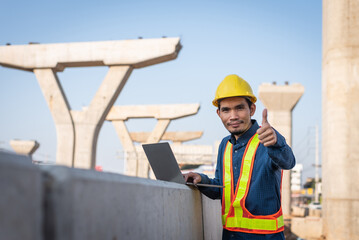 Male engineer standing and thumb up at road construction site with the laptop.