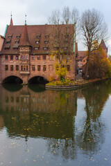 Fototapeta premium Nuremberg landmark. Medieval hospital museum house over canal. Old town of Nuremberg, Germany. Tranquil autumn landscape in old town. Fall season in historical downtown.