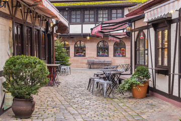 Sidewalk cafe decoration. Outdoor cafe in old town in Germany. Flower pot and street lantern on house facade. Half-timbered decorated house in Nuremberg. Medieval architecture. - 487591788