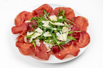 Plate of bresaola with rocket and parmesan in close-up on a white background. Typical Italian food.