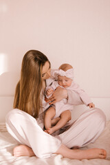 Naklejka na ściany i meble Loving smiling young mother with her newborn daughter on a light background