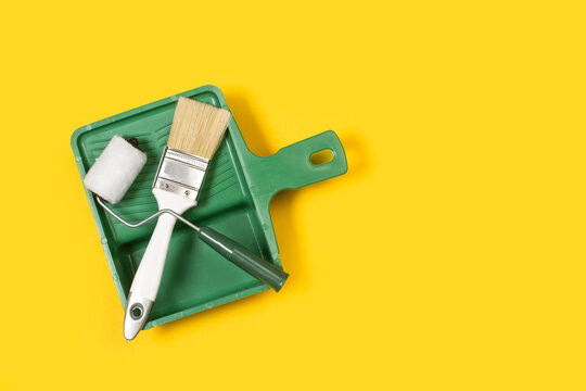 Cubeta de bandeja de pintura verde con pincel y rodillo de pintura sobre un fondo amarillo liso y aislado. Vista superior. Copy space. Concepto de renovaci&oacute;n. Composici&oacute;n minimalista 