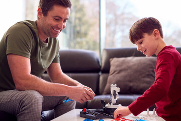 Father And Son Wearing Pyjamas Building Robotic Arm From Plastic Kit At Home