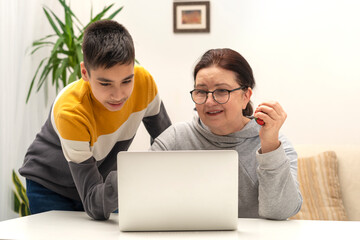 Young boy helps his grandmother or mother deal with the laptop in the room.