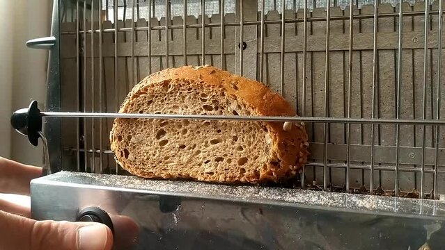 Vertical toaster seen sideways. The holding bar is pulled and a slice of bread placed on the toaster. Power button turned on and filaments begin to glow burning red. Button off and toast removed.