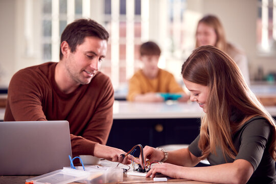 Father Helps Teenage Daughter With Electronics Project Sitting At Kitchen Table At Home With Laptop - Powered by Adobe