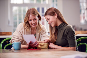 Teenage Daughter Giving Mother Gift And Card As She Sits At Kitchen Table At Home