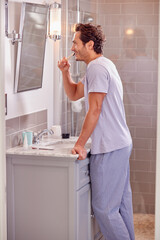 Man Wearing Pyjamas In Bathroom Brushing Teeth With Sustainable Wooden Toothbrush