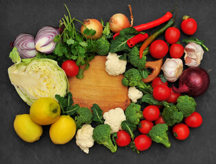 Fresh vegetable salad set , a wooden cutting board in the center .Cabbage, broccoli, cauliflower,cherry tomatoes, onion, cilantro, chili peppers, garlic and lemons on a black background.Top view